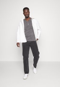 Siva henley majica ispod bijele oversized majice, uparena s tamnosivim trapericama i bijelim tenisicama. Čiste linije i ležeran kroj.