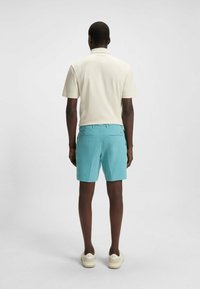Vaaleanbeige polo-paita lyhyillä hihoilla yhdistettynä turkooseihin shortseihin. Shortseissa on sileä pinta ja kaksi takataskua. Valkoiset lenkkarit.
