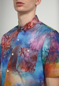 Košile s krátkým rukávem na knoflíky v barevném batikovaném vzoru s odstíny modré, červené a zelené, s jednou náprsní kapsou a límečkem.