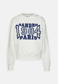 Valkoinen huppari, jossa on tummansininen "Sandro 1984 Paris" -teksti painettuna rasvatuilla, kaarevilla kirjaimilla edessä. Hupparissa on pitkät hihat ja ribbitaskut.