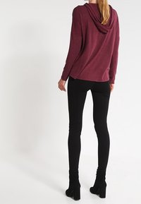 Maroon hooded top with a relaxed fit, paired with black slim-fit pants. The top features a soft texture and a subtle drape at the back.