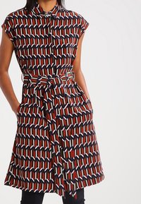 Robe à manches courtes avec un motif géométrique en rouge, marine et blanc, dotée d'un col, d'une taille cintrée et de poches latérales.