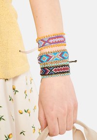 Set med fyra färgglada flätade armband med geometriska mönster i blått, lila, orange och svart, prydda med pärlor och metalliska detaljer.