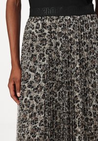 Tiermuster-Faltenrock aus sheer Chiffon, mit einem schwarzen elastischen Bund mit "SPORT"-Text. Die Farben umfassen Beige, Braun und Schwarz.