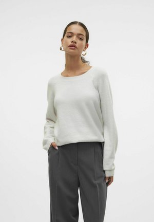 Suéter blanco ligero y texturizado con un escote amplio y mangas largas, combinado con pantalones grises ajustados que presentan un diseño con pliegues.