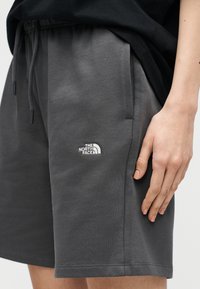 Κοντινό πλάνο προσώπου που φοράει σκούρα γκρι σορτς με κορδόνι και το λογότυπο The North Face κεντημένο στο αριστερό μηρό, καθώς και μαύρο τοπ.