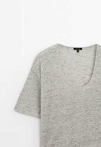 T-shirt gris clair à manches courtes avec un col rond et une texture subtilement tachetée foncée sur un fond blanc uni.