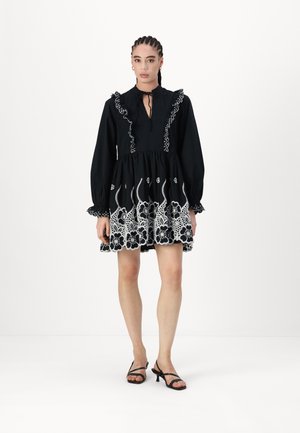 Black dress with white floral embroidery, ruffled neckline, long sleeves, and a flared skirt. Paired with black strappy heels.