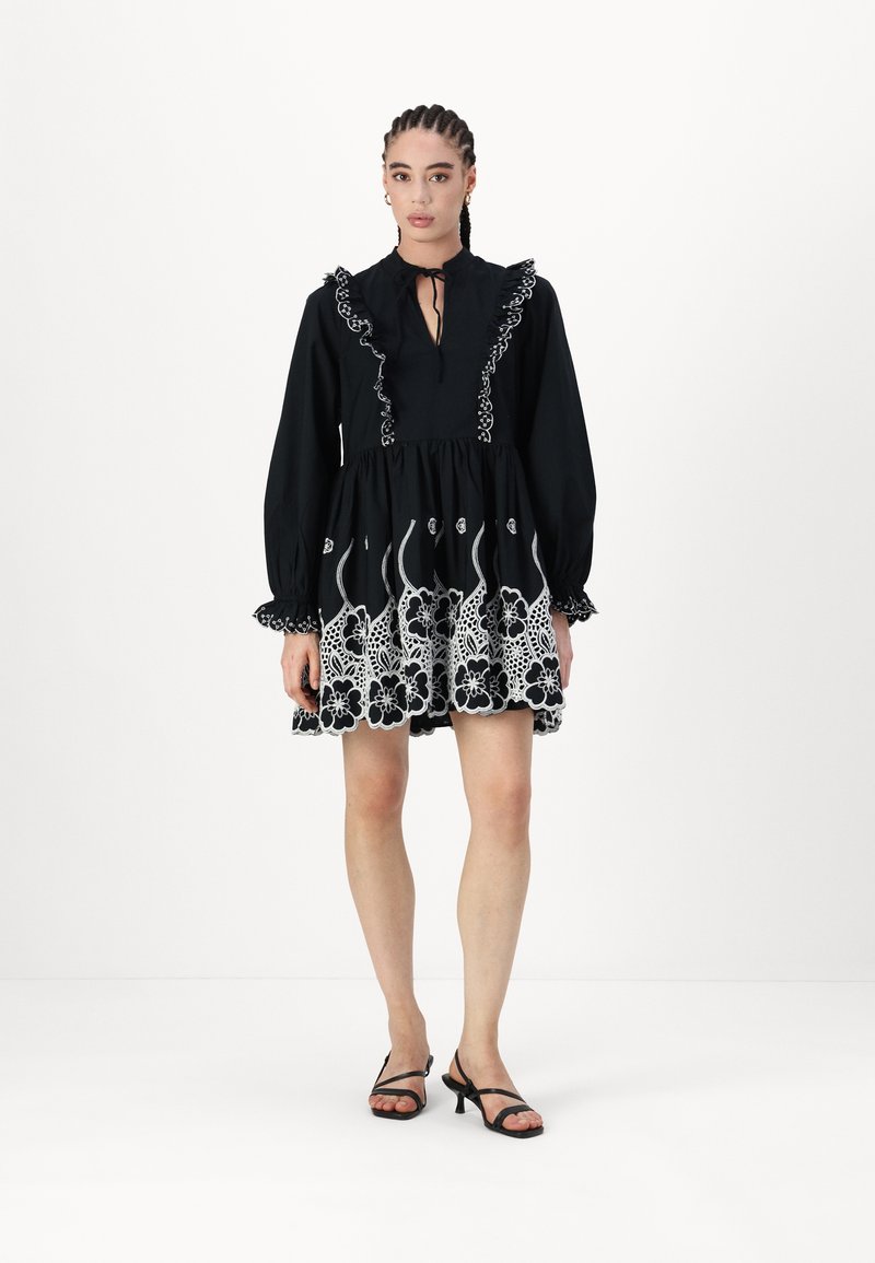 Μαύρο φόρεμα με λευκή floral κεντητική, ριχτό γιακά, μακριά μανίκια και φουσκωτό φούστα. Συνδυάζεται με μαύρες λουρίδες τακούνια.