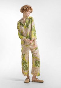 Vævet outfit med grønt og beige bladmønster, lange ærmer, afslappet pasform og elastiske manchetter. Kombineret med lysebrune slip-on sko.