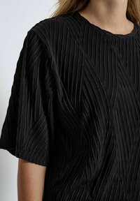 Black short-sleeve top featuring a textured design with raised, diagonal lines. The fabric appears soft and slightly shiny, adding depth.