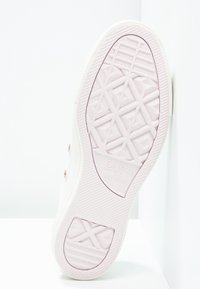 Semelle de chaussure blanche Converse avec motif de grip texturé, présentant un accent rosé sur le caoutchouc. Affiche la marque "Converse All Star".