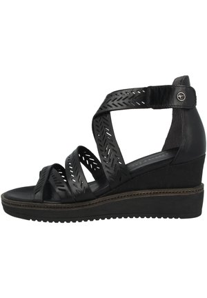 Sorte kilehælssandaler med krydsede remme, der har udskårne mønstre. Sålen har et struktureret mønster og en kontrasterende brun detalje langs kanten.