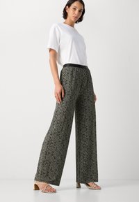 Svart-hvitt mønstrede vide bukser med elastisk linning, sammen med en tettsittende hvit t-skjorte og beige sandaler med stropper.