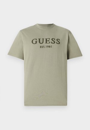 Olive roheline puuvillane T-särk, millel on ümar kaelus ja lühikesed varrukad, ning rinnas tumeroheline tikand "GUESS EST. 1981".