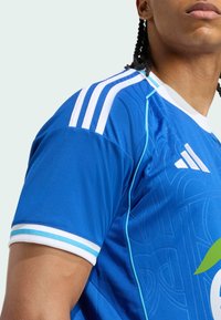 Blaues Sporttrikot mit weißen Akzenten, das drei weiße Streifen auf der Schulter und eine strukturierte Musterung aufweist. Markenlogo sichtbar.