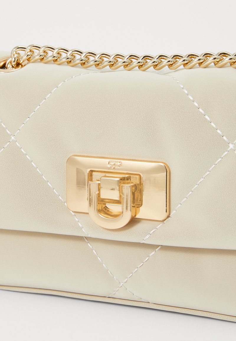 Sac à main en cuir synthétique beige avec une texture matelassée, une bandoulière en chaîne dorée et un fermoir doré avec un design en forme de U.