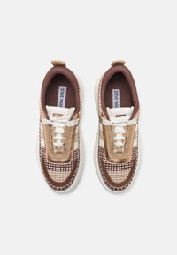 Baskets tricotées beiges et marron avec un motif texturé, lacets blancs, col rembourré et semelle contrastante ; logo sur la languette.