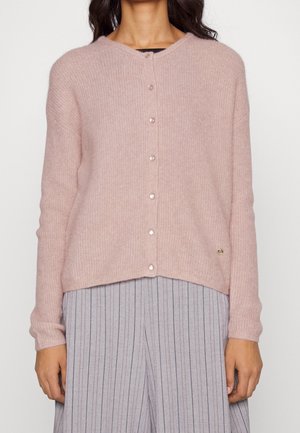 Ljusrosa, stickad kofta med rund halsringning, pärlknappar och en diskret gulddetalj med logotyp på nedre sidan. Matchas med randiga byxor.