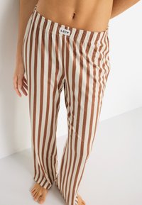 Ριγέ παντελόνες με φαρδιά πόδια σε ανοιχτό μπεζ και καφέ, με ελαστική μέση και λευκή ετικέτα. Μαλακό ύφασμα με απαλή υφή.