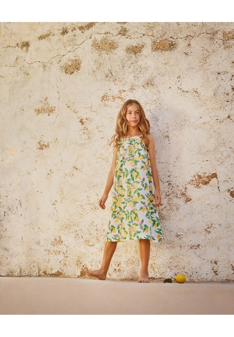 Abito floreale con motivi di limoni e foglie verdi su sfondo bianco. Design senza spalline, lunghezza al ginocchio, realizzato in tessuto leggero.