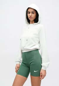 Ανοιχτό γκρι φούτερ με κουκούλα και κορδόνια, με λογότυπο Nike, συνδυασμένο με πράσινα εφαρμοστά σορτς που διαθέτουν λευκό λογότυπο Nike swoosh. Ομαλές υφές.