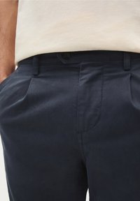 Chinos blu navy in cotone con una consistenza liscia, dotati di pieghe frontali, chiusura con bottone e tasche laterali.