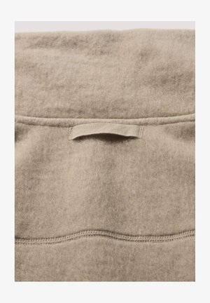 Beige wolweefsel met een zachte, gestructureerde oppervlakte. Bevat een horizontale naad en een kleine stoffen lus in het midden bovenaan voor gemakkelijke handling.