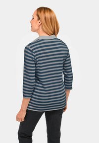 Dreiviertelarm-Bluse in Marineblau und Graustreifen, mit einem einfarbigen Kragen. Aus weichem Stoff und lockerer Passform, kombiniert mit dunklen Hosen.