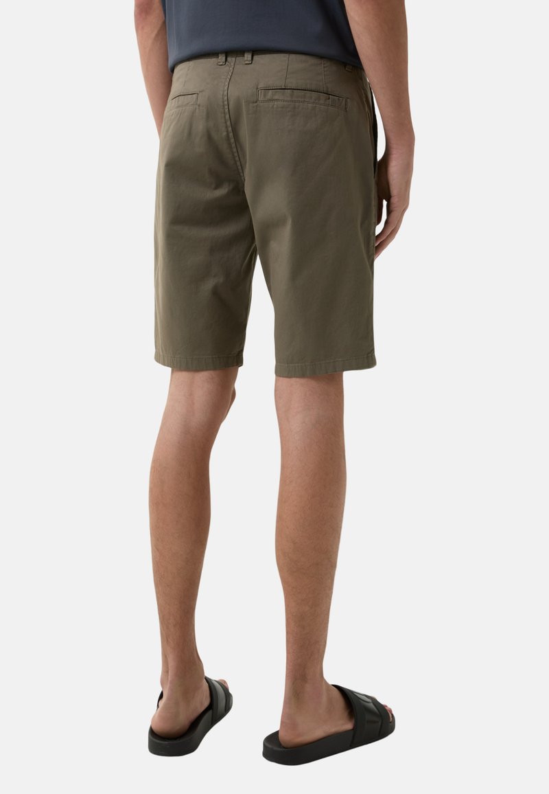 Olivgrüne Shorts aus Baumwolle mit geradem Schnitt, Gesäßtaschen und dezenten Nähten. Getragen mit schwarzen Sandalen.