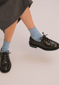 Scarpe in pelle nera con punte arrotondate, lacci decorativi e suola spessa. Indossate con calze a coste blu chiaro e una gonna grigia.