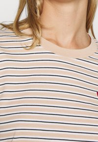 Randig kortärmad skjorta i persika, svart och vitt. Har en rund halsringning och en liten broderad detalj på bröstet. Mjuk textur.