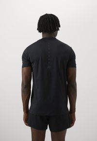 T-shirt de sport noir à manches courtes, en tissu texturé, avec un col rond et une rangée de boutons dans le dos, associé à un short noir.