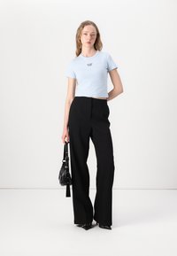 Lys blå cropped t-skjorte med svart tekst, kombinert med høyhalsede svarte vide bukser. Modellen bærer en liten svart håndveske.