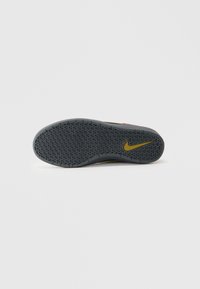 Sola de sapato Nike em borracha cinza, apresentando um padrão em ziguezague e um logótipo swoosh amarelo. O design enfatiza a tração e a durabilidade.