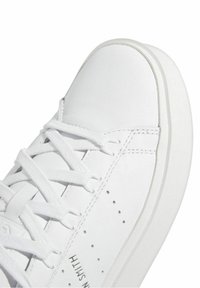 Vita sneakers i slät läder. Har platta snören, perforeringar för andningsförmåga och en texturerad gummisula.