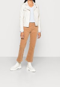 Vit läderbikerjacka, ljusblå stickad topp, beige kordflöjelbyxor med utsvängda ben och vita kraftiga ankla stövlar med en texturerad sula.