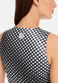 Black sleeveless top with a white polka dot pattern. Features a round neckline and a small logo near the back. Smooth texture.