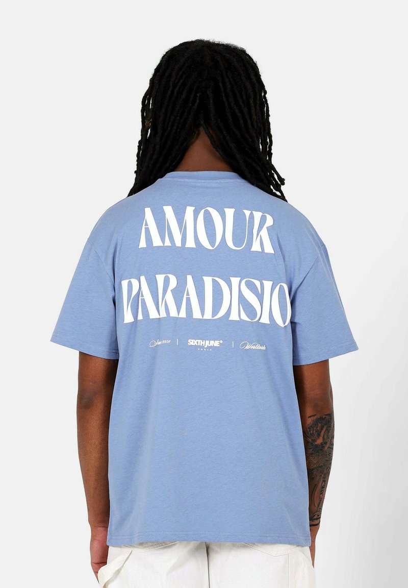 Lichtblauwe katoen t-shirt met een groot wit grafisch ontwerp met "AMOUR PARADISIO" op de achterkant. Korte mouwen, ronde hals.