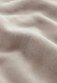 Țesătură de culoare bej deschis, cu o textură netedă și un model de tricotaj fin, care prezintă falduri delicate și un luciu subtil pe suprafață.