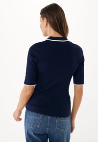 Granatowa koszulka polo z krótkim rękawem z prążkowanej tkaniny, z białymi wykończeniami kołnierzyka i rękawów oraz falbanką na dolnym brzegu.