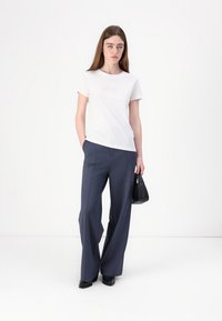 White cotton t-shirt with a subtle embroidered detail, paired with high-waisted, wide-leg navy trousers. Black handbag completes the outfit.