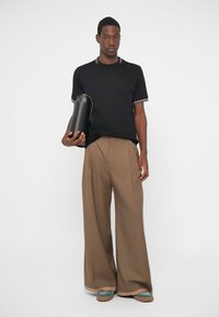 Melns īsām piedurknēm krekls ar daudzkrāsainu svītru apkakli, plata brūna bikses un kurpes ar tirkīza akcentiem; tur melnu cilindrisku somu.