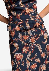 Blumiges Peplum-Top aus dunkelblauem Stoff mit lebhaften roten und cremefarbenen Blumen. Mit plissierten Akzenten um die Taille für zusätzlichen Detailreichtum.