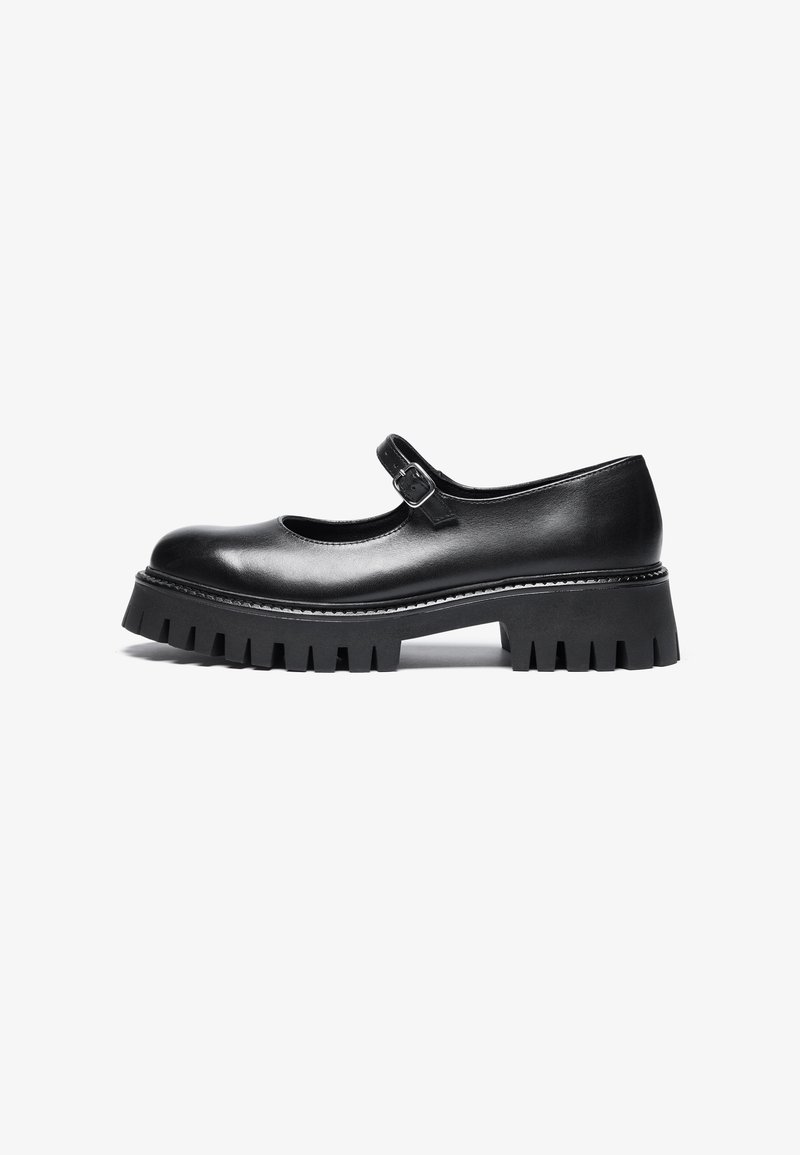 Chaussure Mary Jane en cuir noir avec semelle crantée épaisse et bride réglable à boucle, vue de profil sur fond blanc.