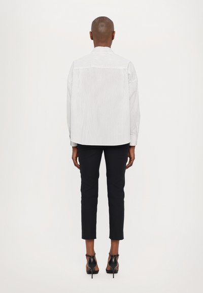 Gestreept overhemd in wit en lichtblauw, relaxed fit, gecombineerd met zwarte cropped broek en hoge hakken, gezien van achteren.
