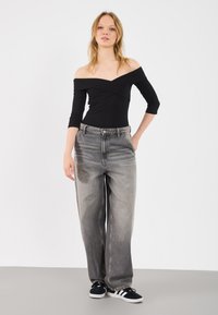 Top negru, cu umerii goi, slim fit, asortat cu blugi din denim gri, cu talie înaltă și croi larg, având un aspect ușor decolorat și o textură subtilă.