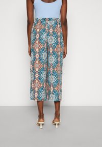 Culottes à motifs avec des designs floraux bleus, oranges et blancs. Tissu léger, coupe ample, longueur mi-mollet, et taille élastique.