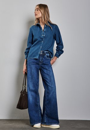 Dark blue denim shirt with a button-up design and long sleeves, paired with wide-leg dark blue jeans. Equipped with a brown textured handbag.
