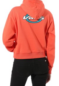 Hoodie corto corallo in morbido cotone, con un logo circolare blu di Vans sulla schiena. Include un cappuccio e orlo a coste con tasche laterali.